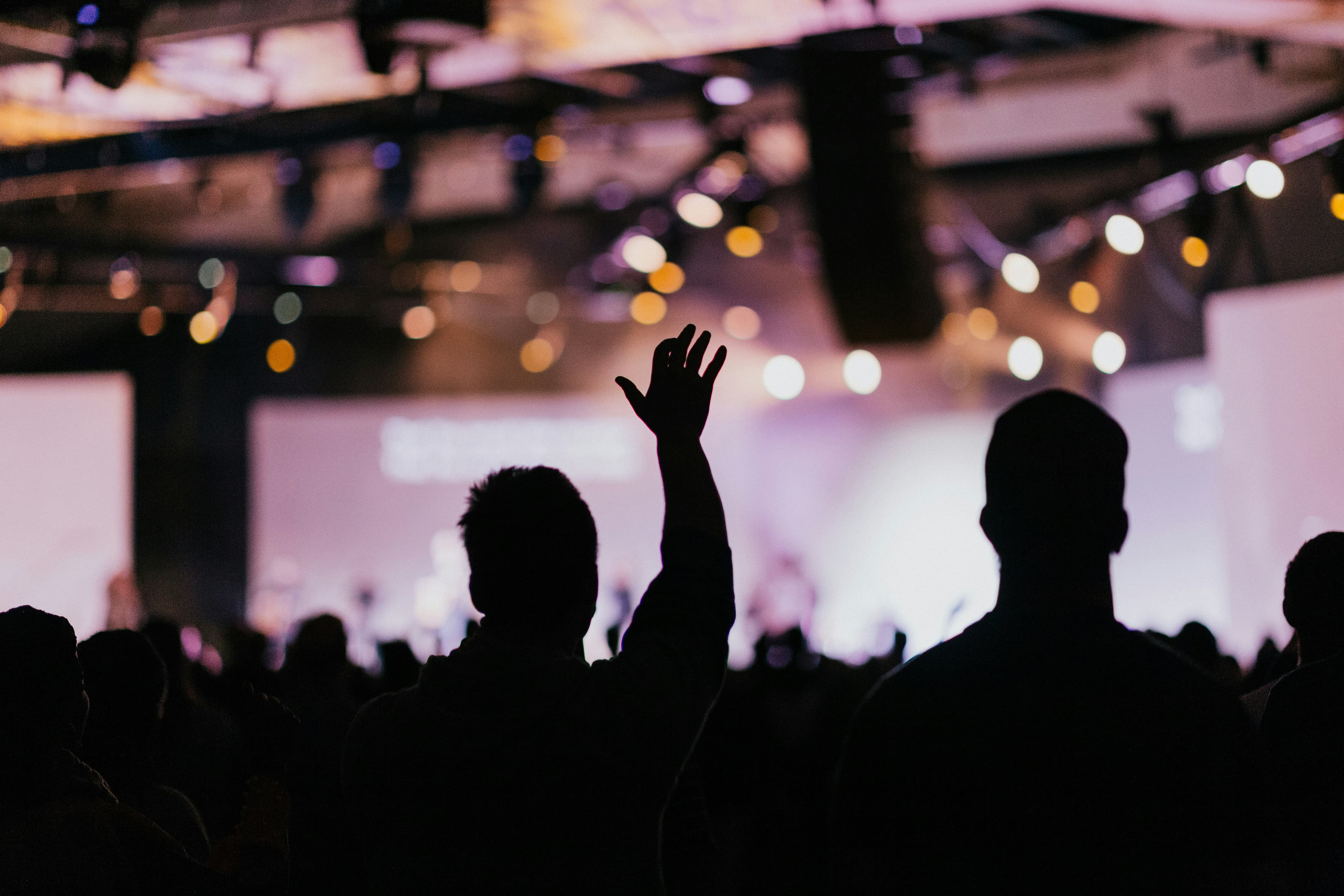 A silhouette of an audience with one raised hand with.